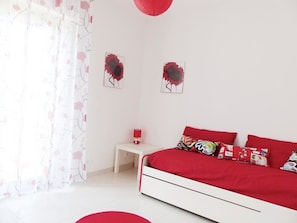Un dormitorio con una cama blanca, ropa de cama roja y una mesita de noche con una lámpara roja.