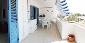 A balcony with a white table and chairs, a potted plant, and a view of the surrounding area. - Casa Vacanza Gli Ulivi (Santa Croce Camerina)