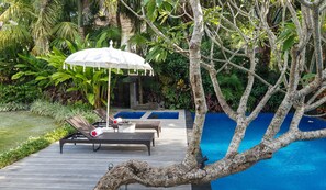 A poolside area with lounge chairs, a covered umbrella, and a wooden deck.