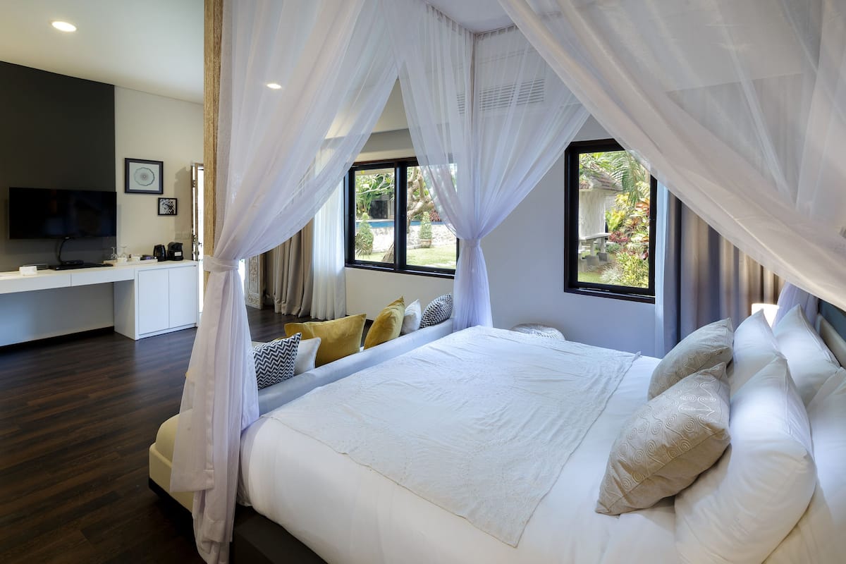 Quarto com cama, televisão, escrivaninha e janela com vista para o verde.