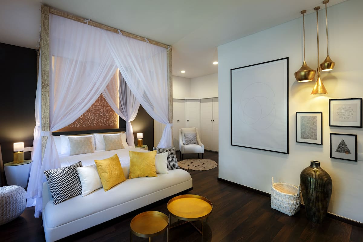 Um quarto moderno com cama de dossel, mesas de cabeceira, um sofá, um vaso grande e obras de arte na parede.
