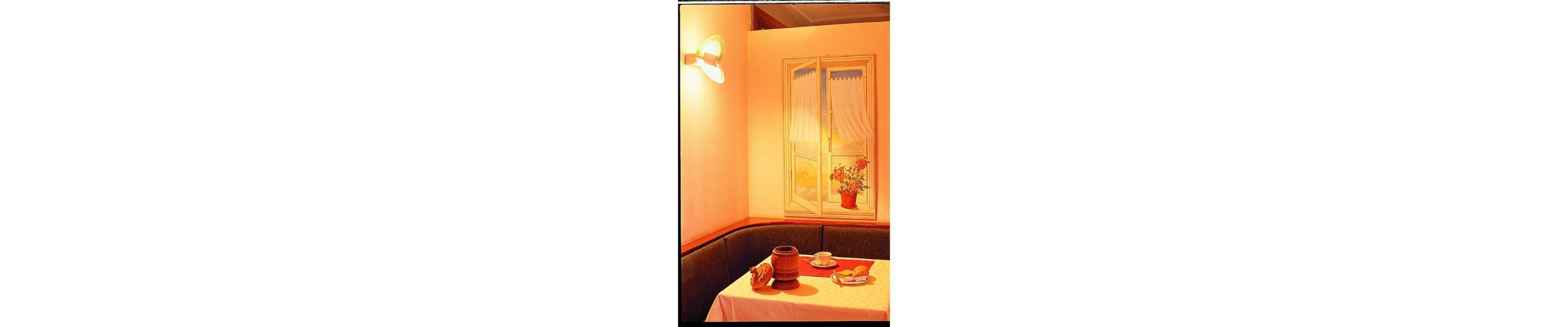 A corner of a room with a table set for a meal, a window with curtains, and a wall-mounted light fixture.