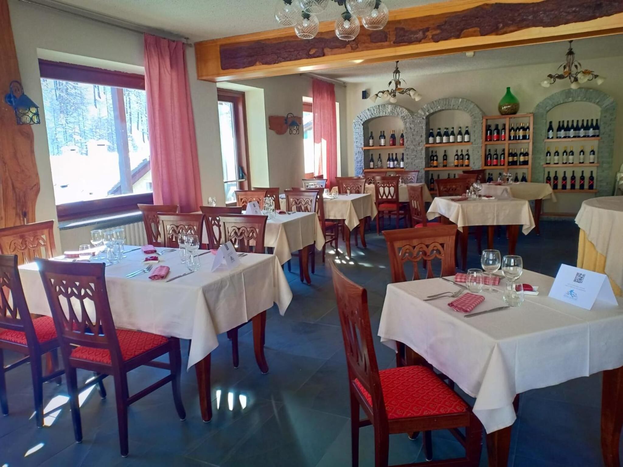 Un restaurant doté de nombreuses tables et chaises, d’un présentoir à vin et offrant une vue sur les arbres à l’extérieur.