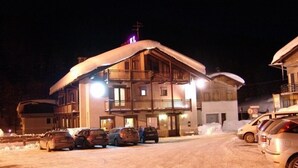 Un edificio cubierto de nieve con un balcón y varias ventanas, rodeado de coches aparcados y nieve.