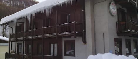 Un hotel con balcón, un cartel que indica que es un hotel y una montaña nevada al fondo.