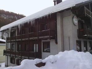 A hotel with a balcony, a sign indicating it is a hotel, and a snowy mountain in the background.