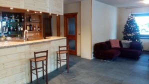 Una cocina con barra, una mesa de comedor con sillas, un sofá de color oscuro y un árbol de Navidad.