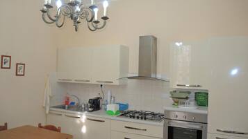 A kitchen with white cabinets, a gas stove, an oven, a chandelier, and a dining table with chairs.