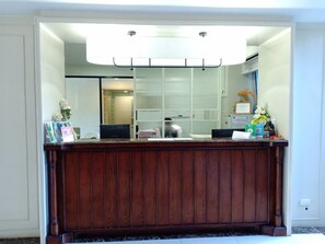 Un comptoir d’accueil avec un revêtement en bois, un luminaire moderne au-dessus et un miroir qui reflète l’intérieur.