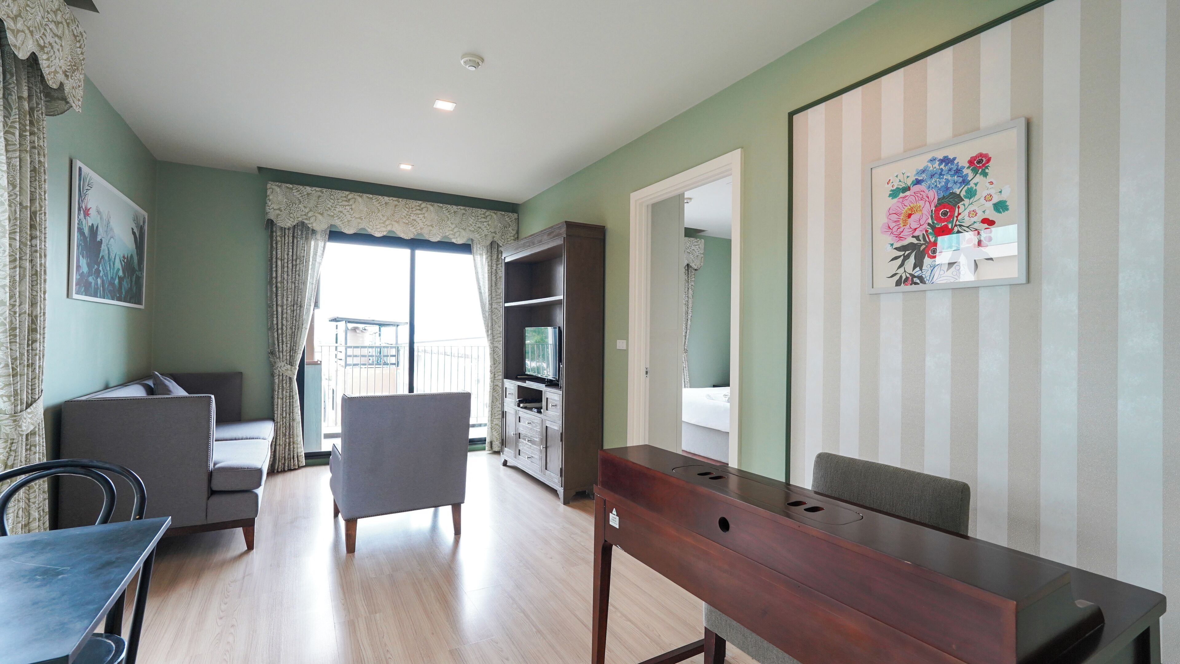 A hotel room with a balcony, a dining table, a sofa, and a TV.