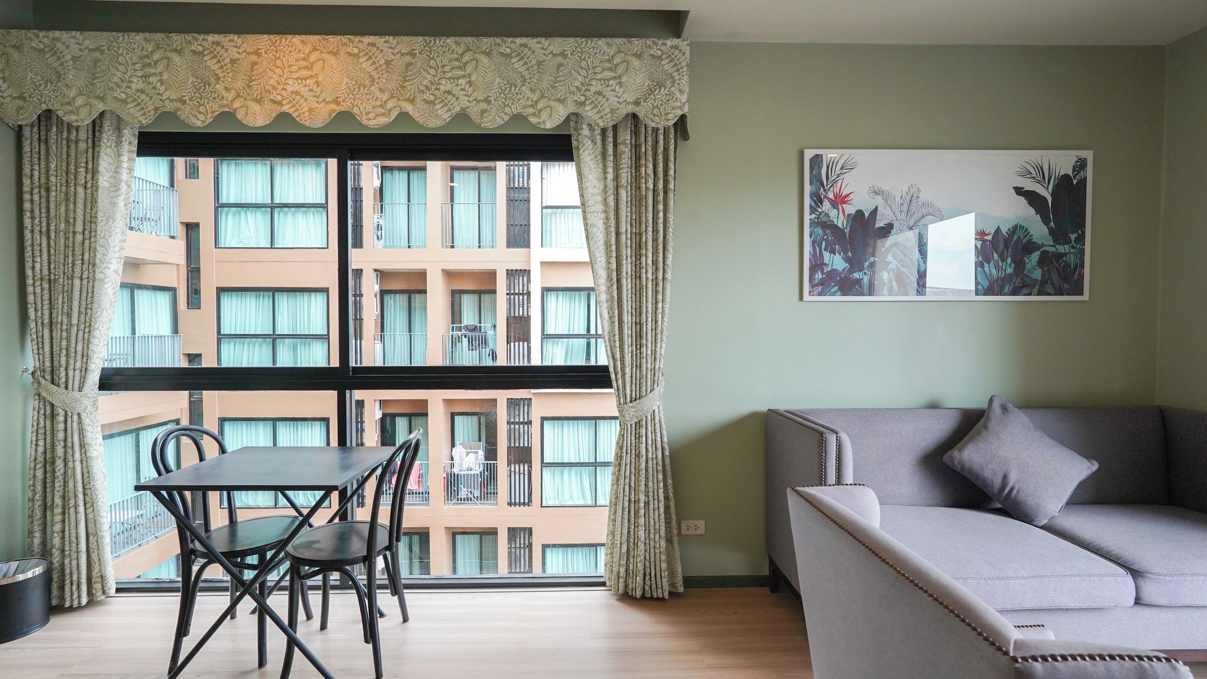Une pièce comprenant une table à manger et des chaises, un canapé, une fenêtre avec des rideaux et un tableau accroché au mur.