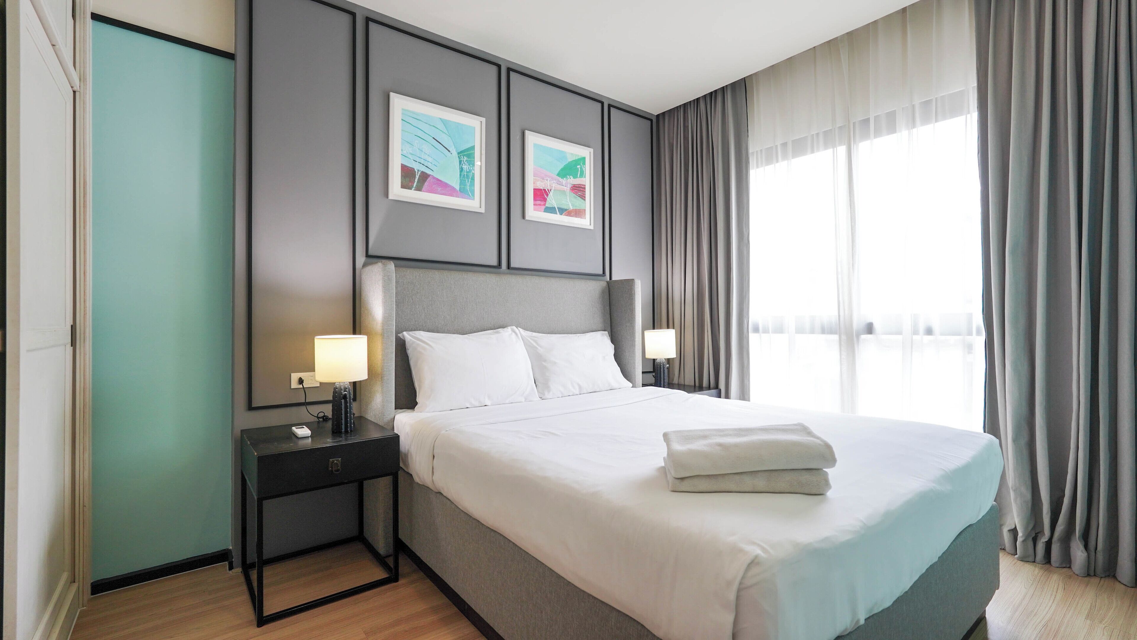 A hotel room with a bed, nightstands, a lamp, a wall-mounted artwork, and a window with curtains.