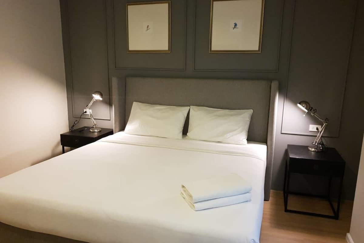 Una cama bien hecha con sábanas blancas, dos mesitas de noche con lámparas y dos cuadros en la pared.