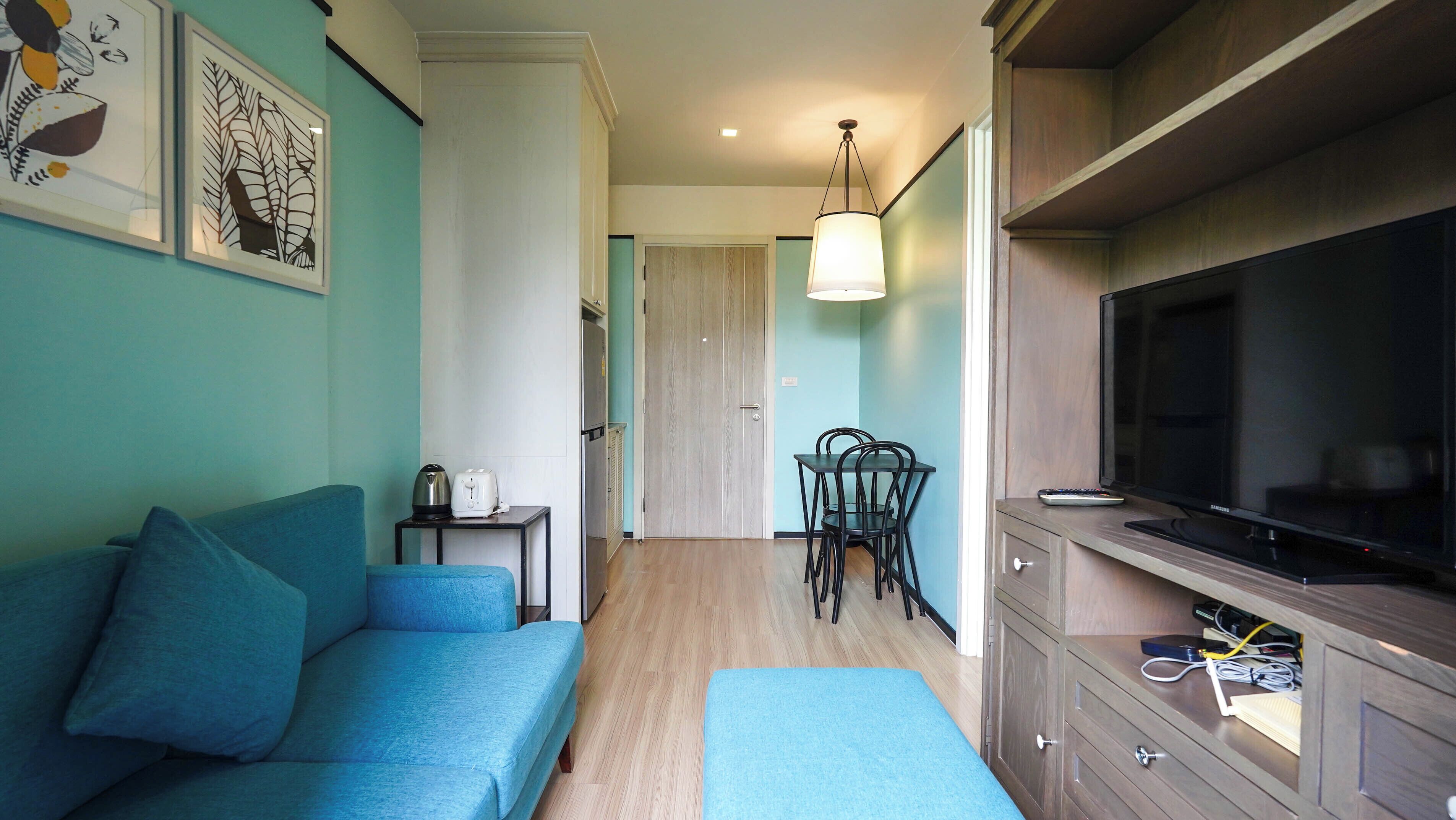Un espacio habitable compacto con sofá, una mesa de comedor con sillas, televisor y una zona de kitchenette.