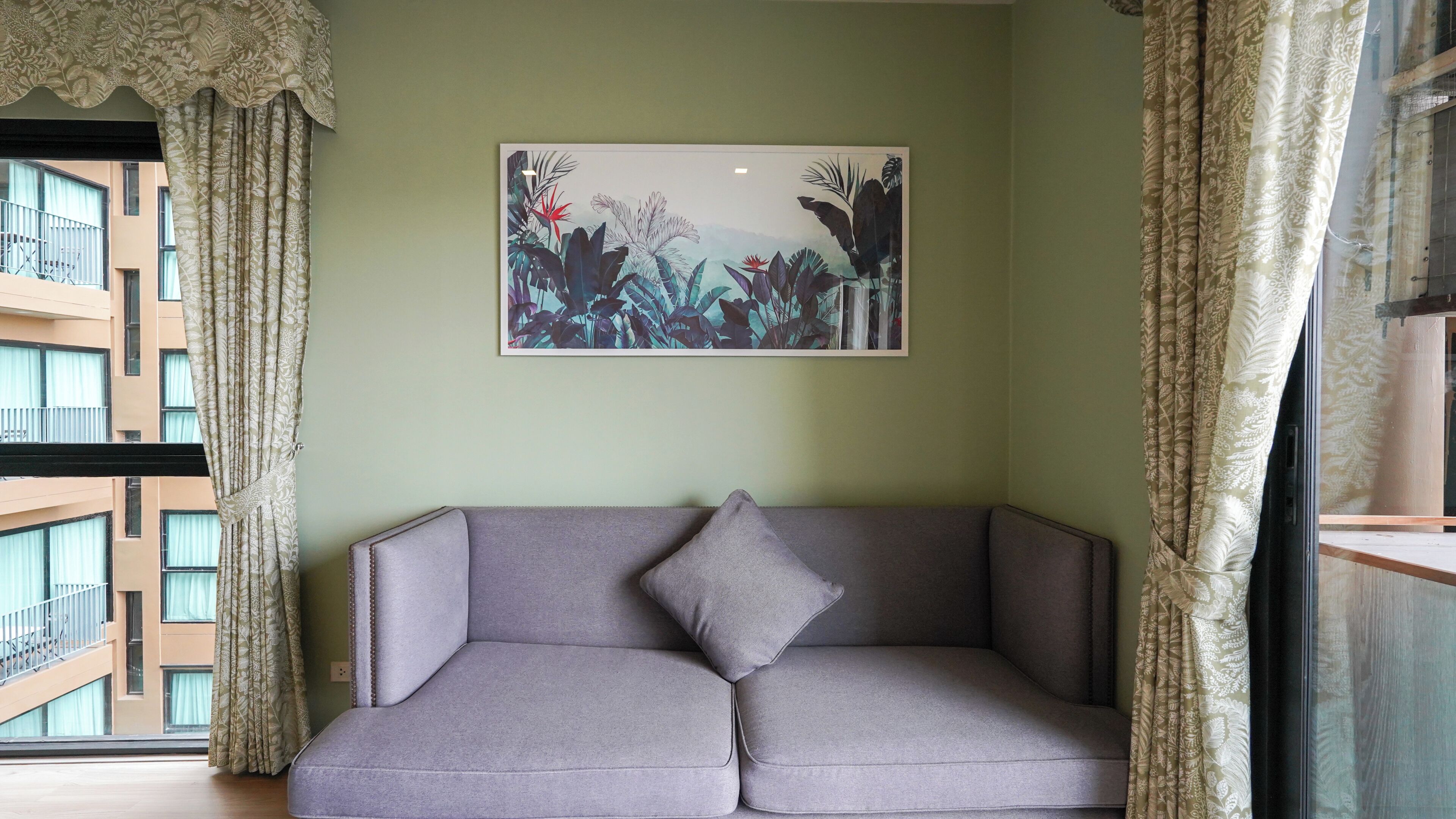 Une pièce avec un canapé gris, une estampe botanique encadrée au mur et des rideaux à motifs.