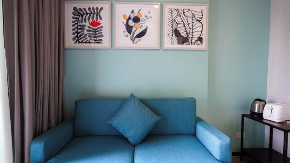 A room with a blue sofa, a framed floral artwork on the wall, a kettle, and a toaster on a small table.