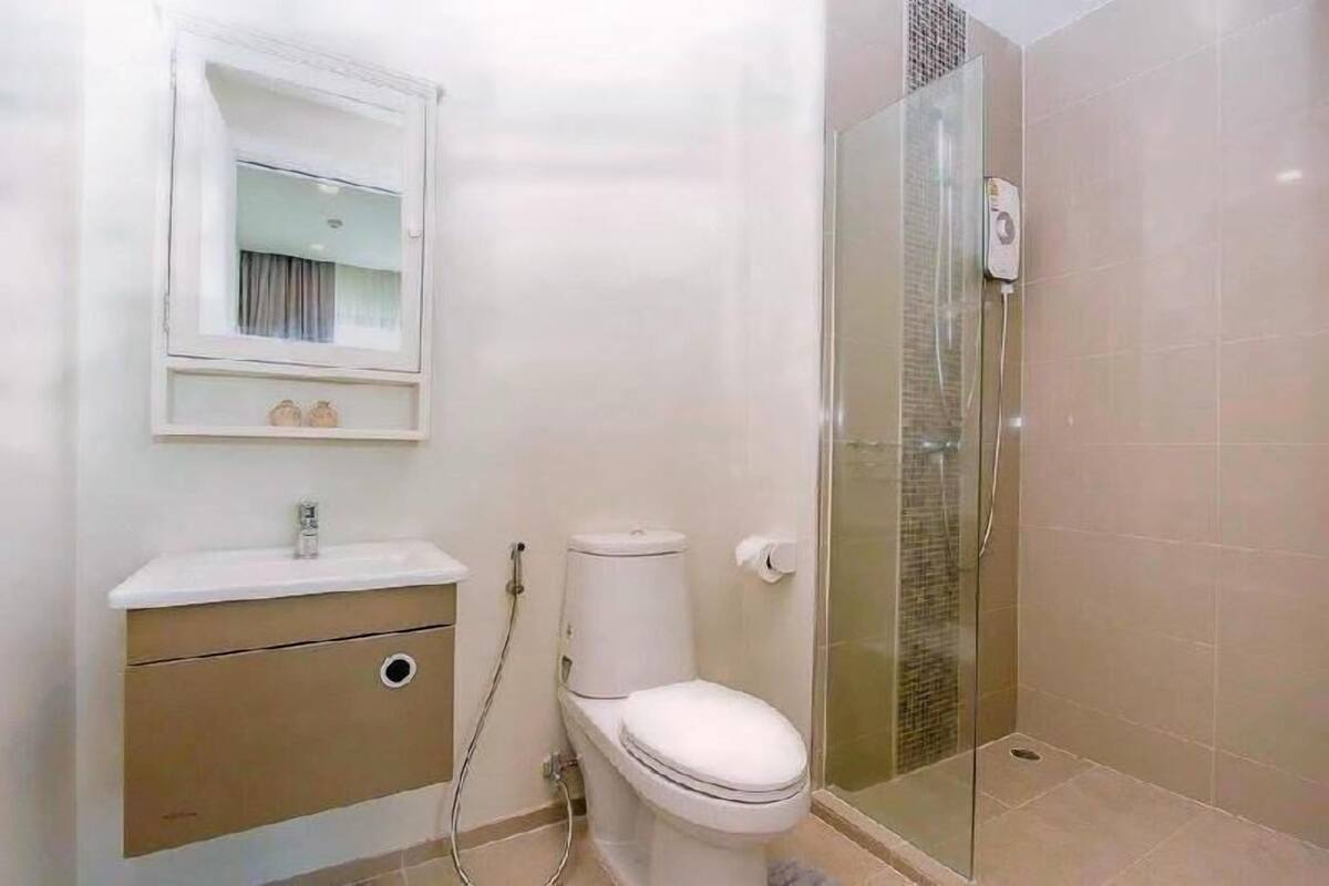 A bathroom with a toilet, sink, mirror, and glass shower enclosure.