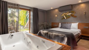 Un dormitorio moderno con una cama grande, una bañera y vistas a la vegetación exterior.