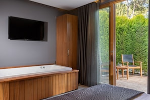 Un baño moderno con una bañera de madera, un espejo grande y un televisor de pantalla plana en la pared.