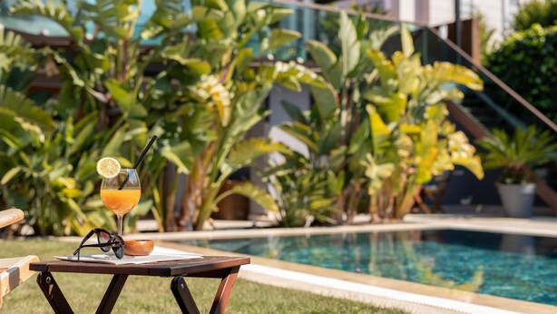 Escena junto a la piscina con un vaso de jugo de naranja, un par de gafas de sol y un cuenco de madera sobre una mesa.