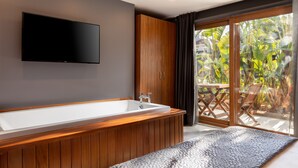 Un baño moderno con tocador de madera, una bañera grande y un televisor de pantalla plana en la pared.
