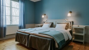 Un dormitorio con una cama doble, dos mesitas de noche, una ventana con cortinas y una lámpara de pared.