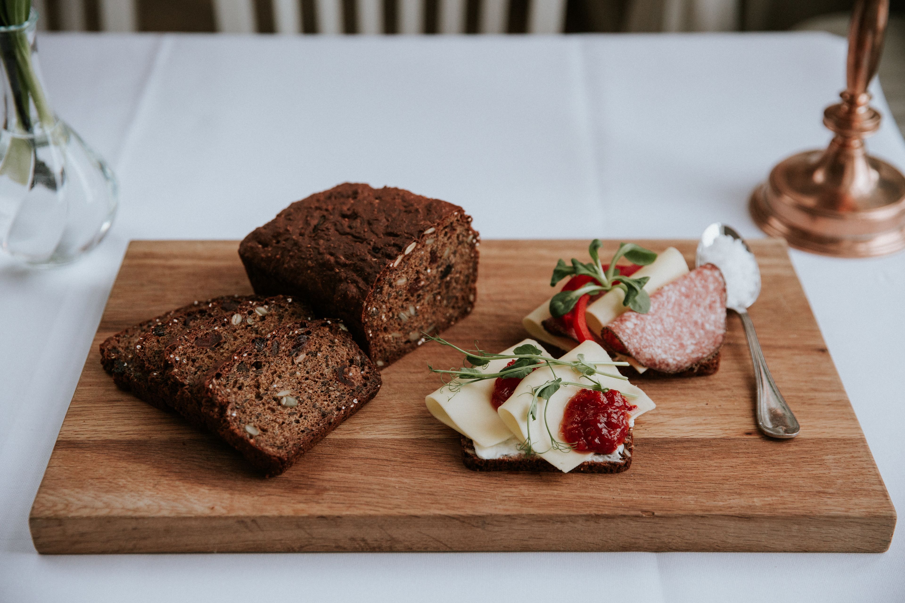 A wooden board with slices of dark bread, a piece of cheese, and a small salad on a white tablecloth.