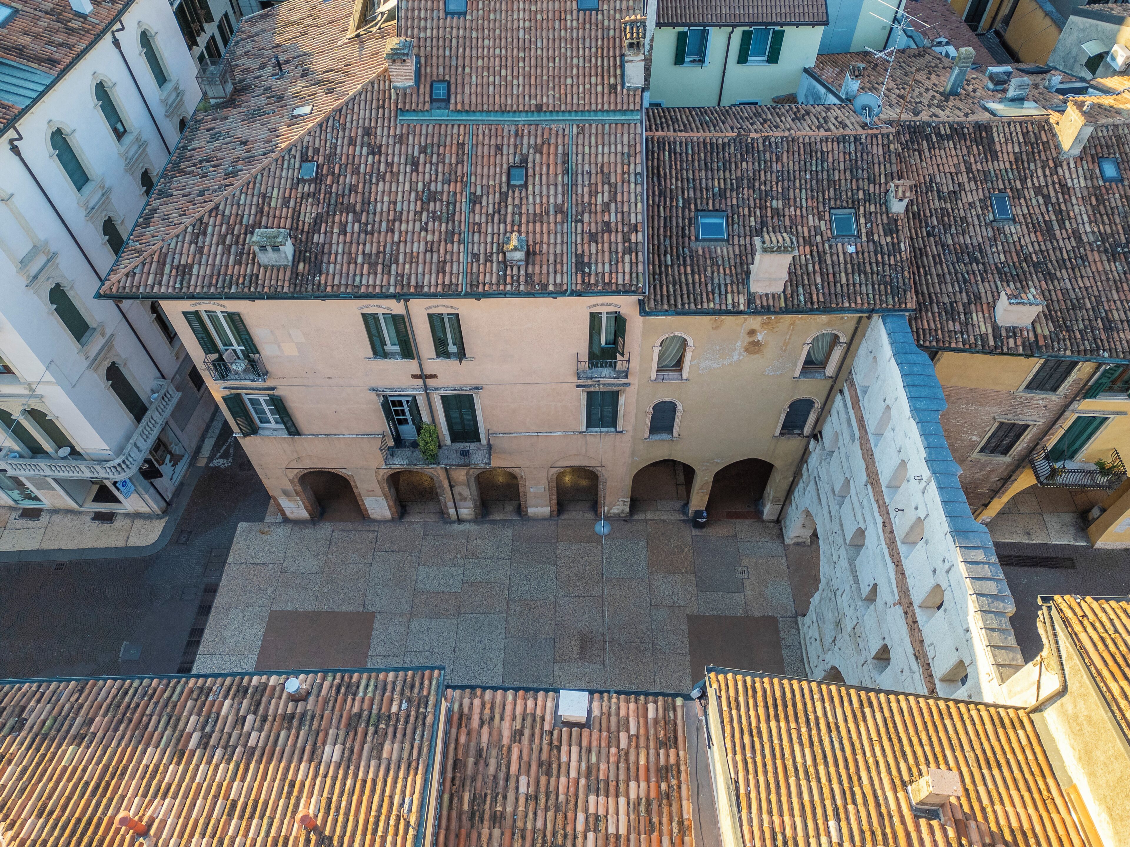 An aerial view of a historic building with a courtyard, featuring a central archway and a tiled roof.