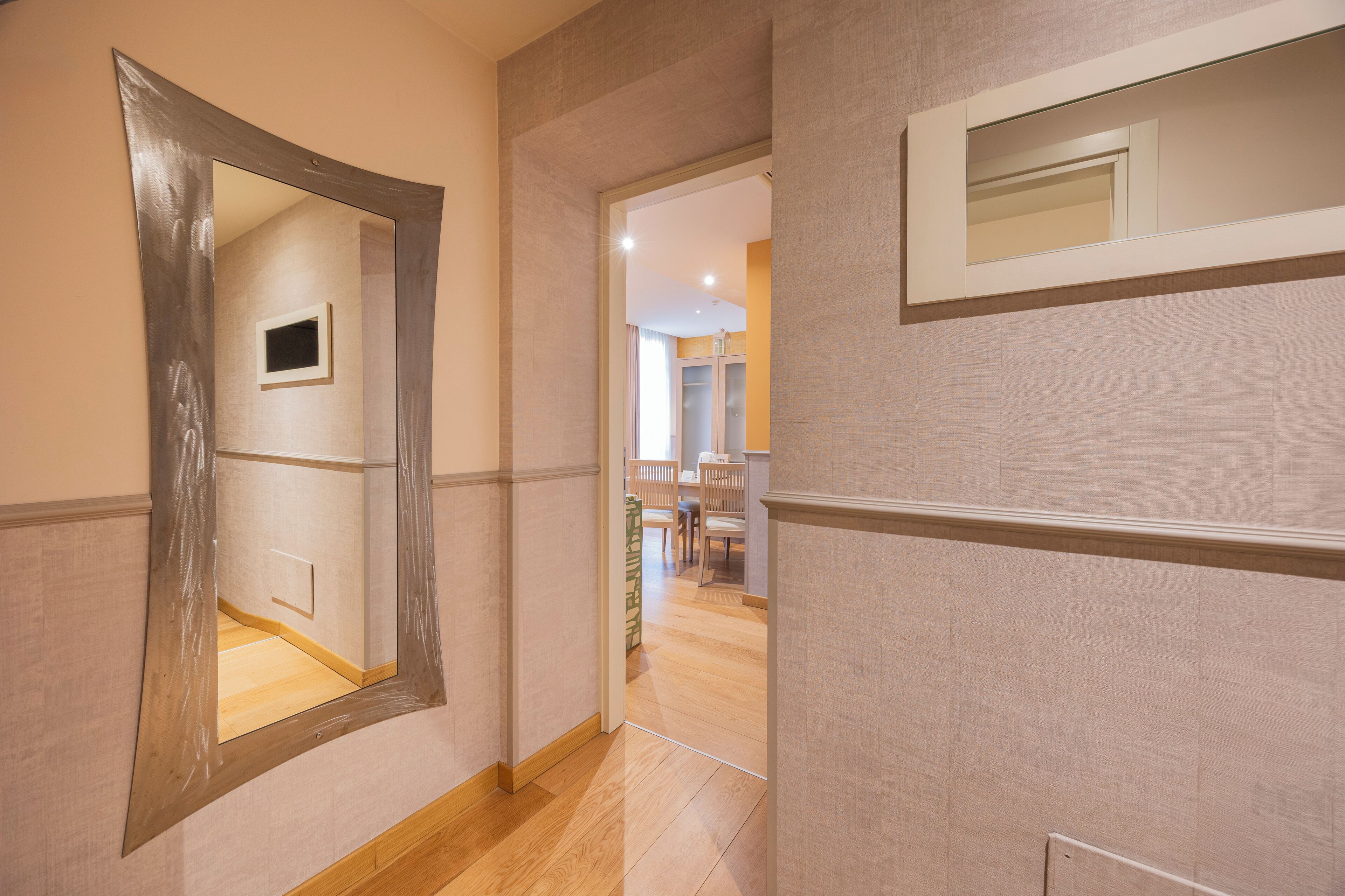 Un couloir avec un grand miroir, un plancher en bois et une porte donnant sur une salle à manger.