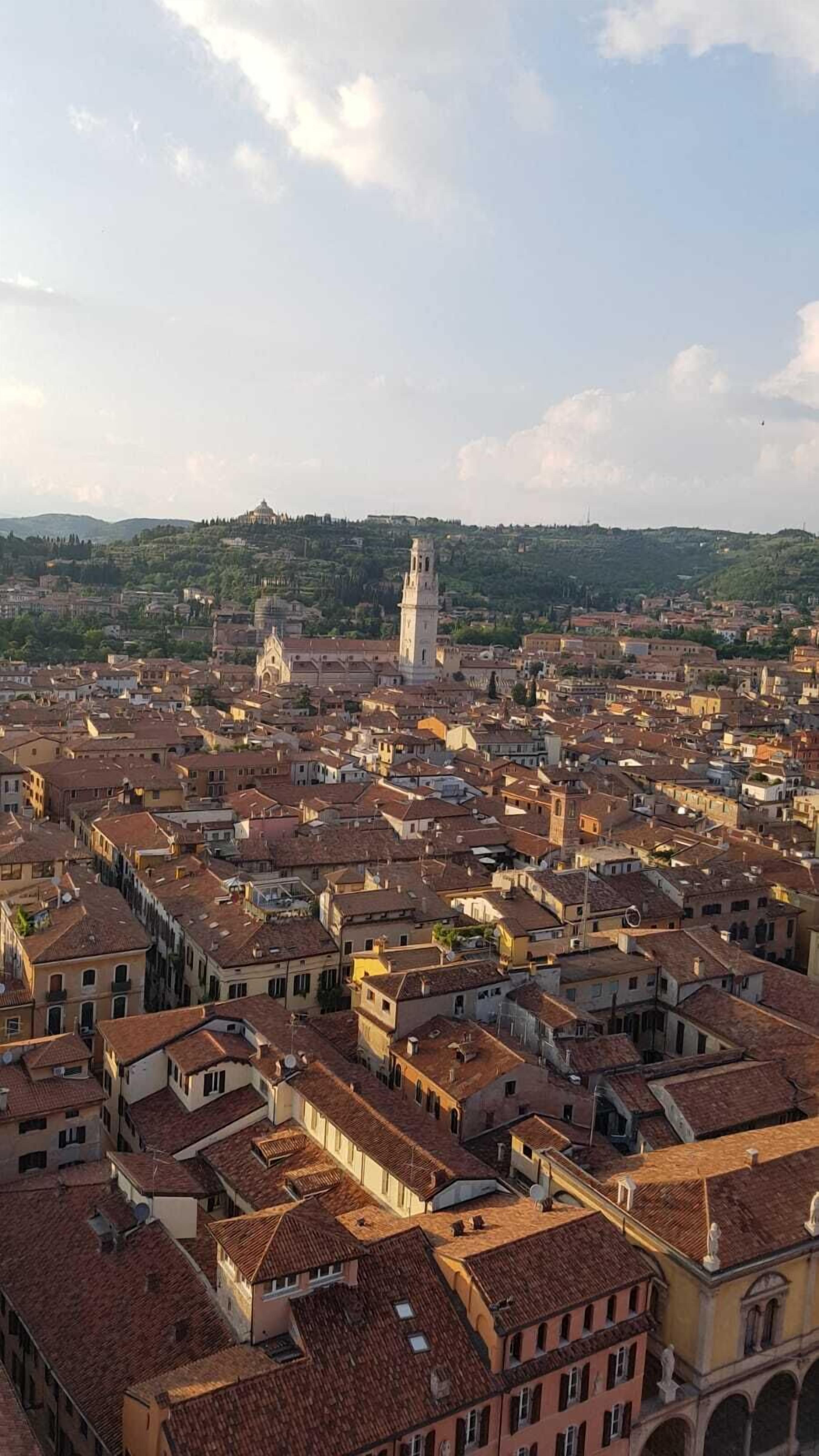 Vista panorâmica de uma área urbana densamente povoada com arquitetura histórica, incluindo uma torre imponente e uma catedral ao longe.