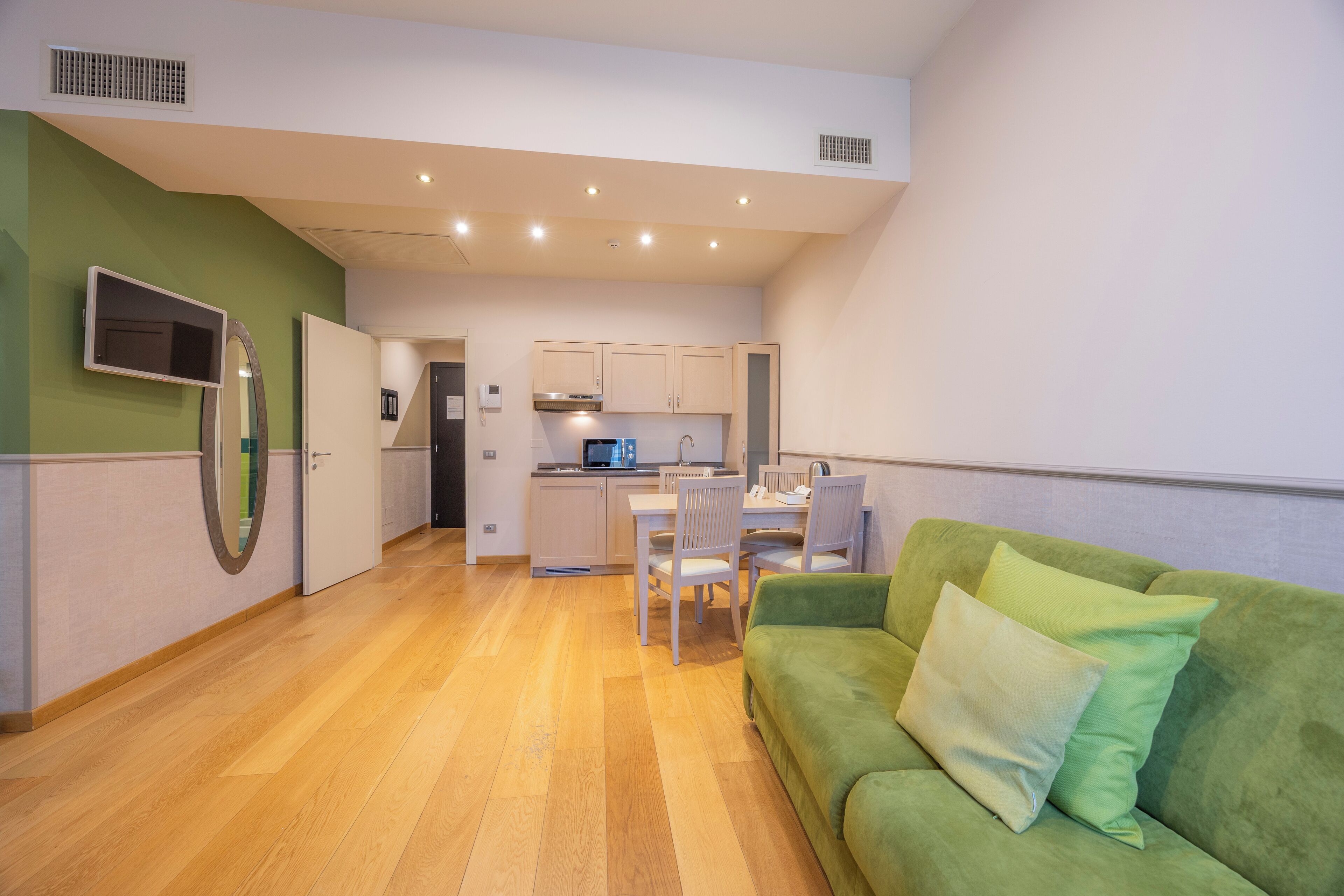 A modern kitchen with white cabinets, a dining area with a table and chairs, and a green sofa with pillows.