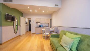 A modern kitchen with white cabinets, a dining area with a table and chairs, and a green sofa with pillows.