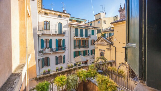 A narrow alleyway with buildings on either side, featuring balconies with plants and a wrought iron gate. - Residenza Palazzo Negri (Verona)