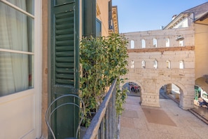 A stone bridge with arches, a balcony with a metal railing, and a building with a window and shutters. - Residenza Palazzo Negri (Verona)