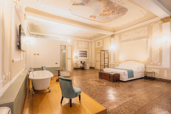 A spacious room with a large bathtub, a wooden bench, a bed, and a desk with a chair. - Residenza Palazzo Negri (Verona)