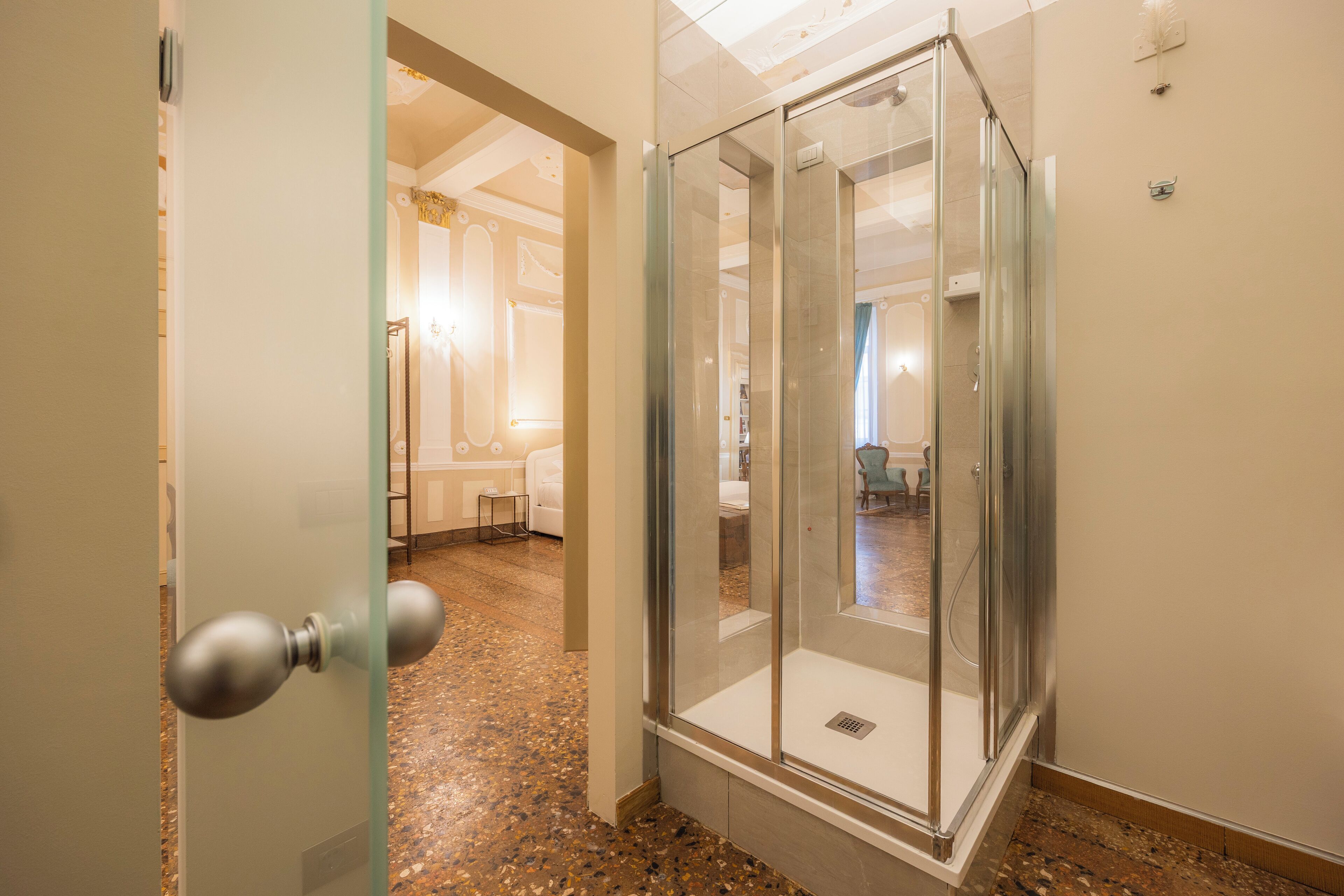 A hotel room with a glass-enclosed shower, a marble floor, and a view into the adjacent living area.