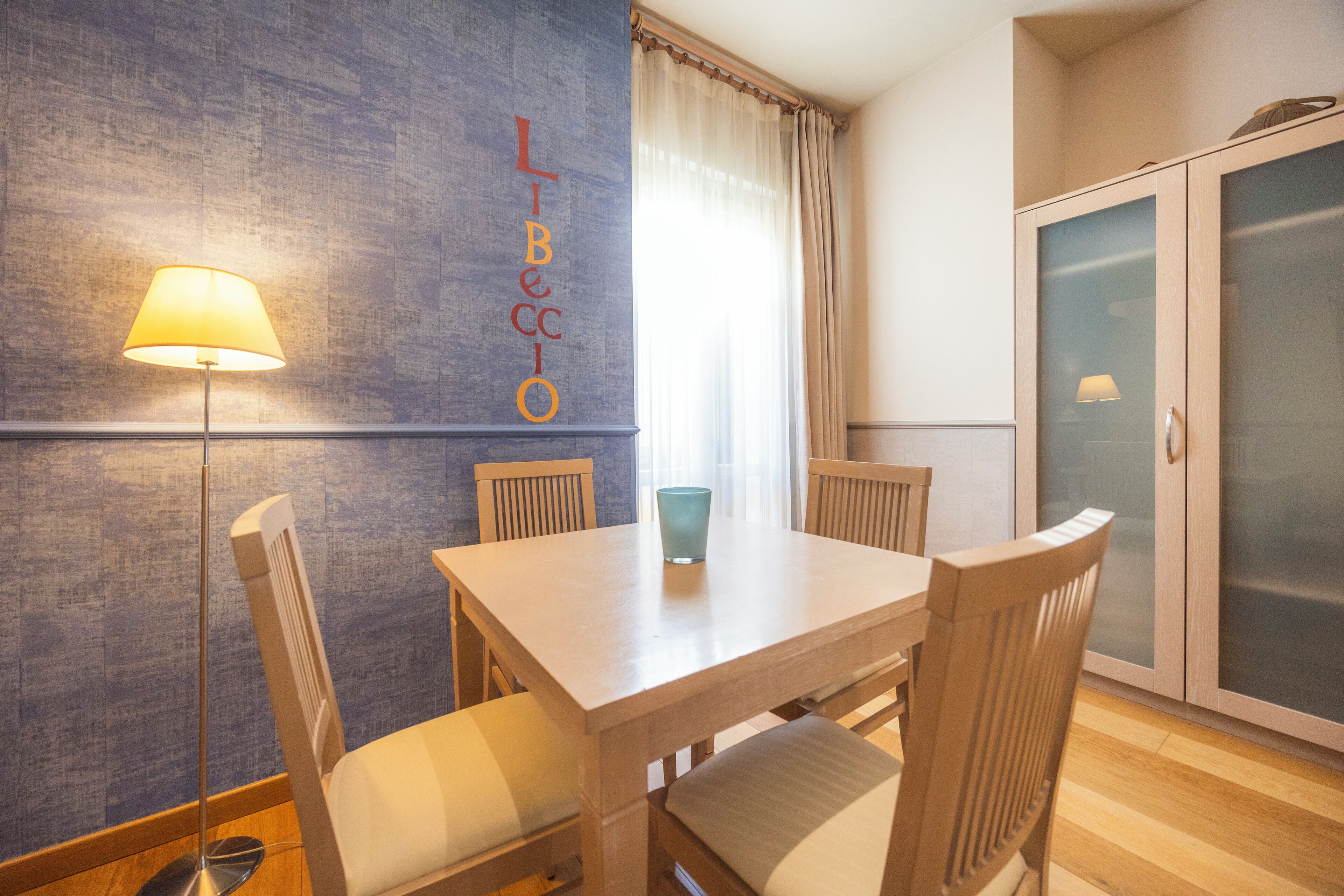 A dining area with a table and chairs, a lamp, and a cabinet with frosted glass doors.