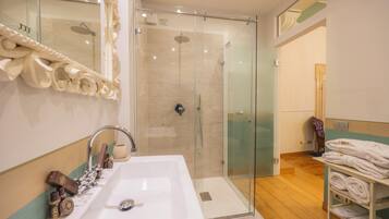 A modern bathroom with a large white sink, a glass shower enclosure, and a towel rack with neatly folded towels.