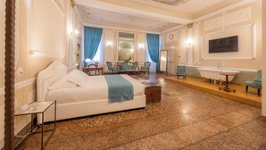 A spacious bedroom with a large bed, a sitting area with chairs, a vanity with a mirror, and a bathtub. - Residenza Palazzo Negri (Verona)