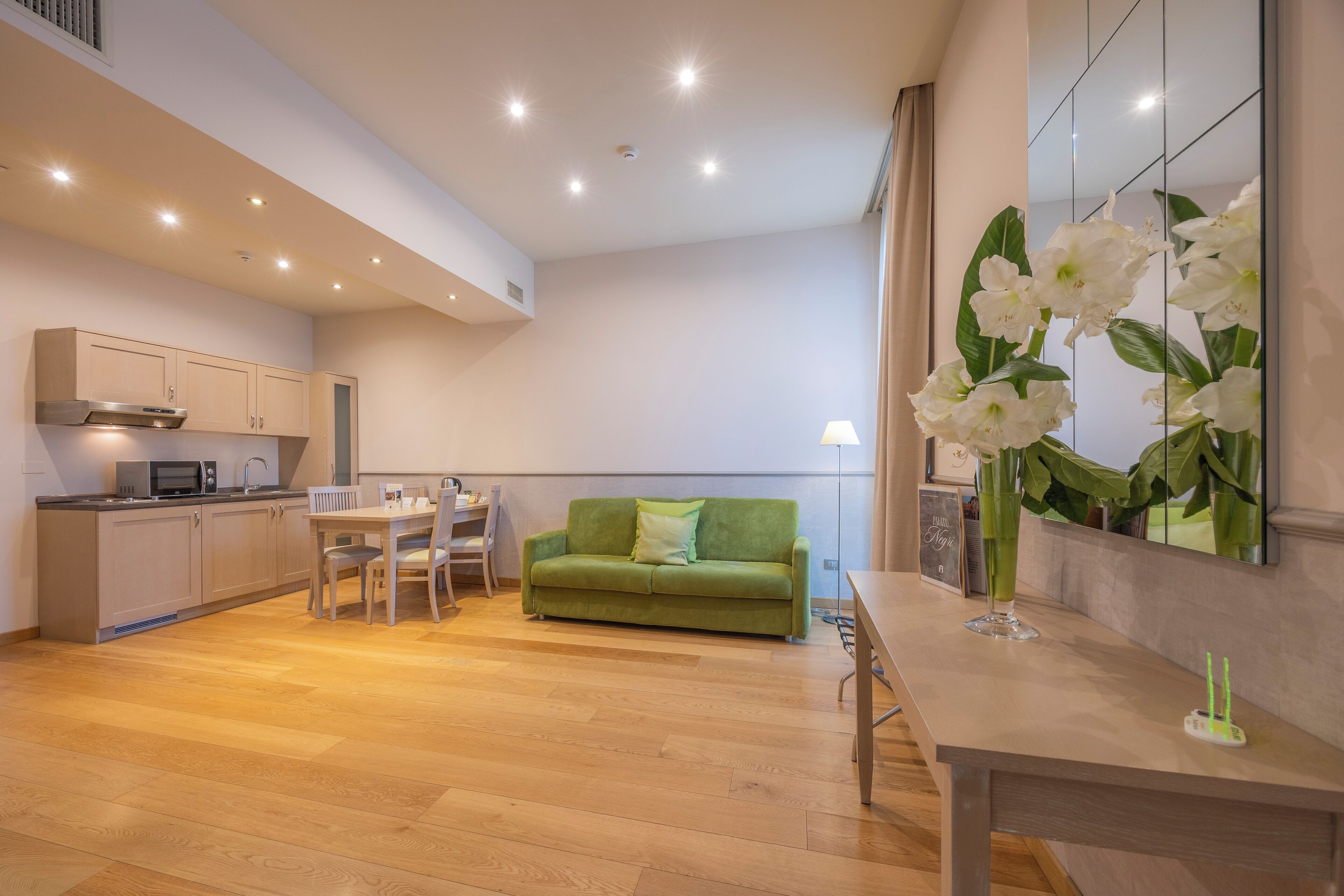 Ein modernes Wohnzimmer mit einem grünen Sofa, einem Holzespeisetisch und einer Küchenzeile mit Schränken und einer Mikrowelle.