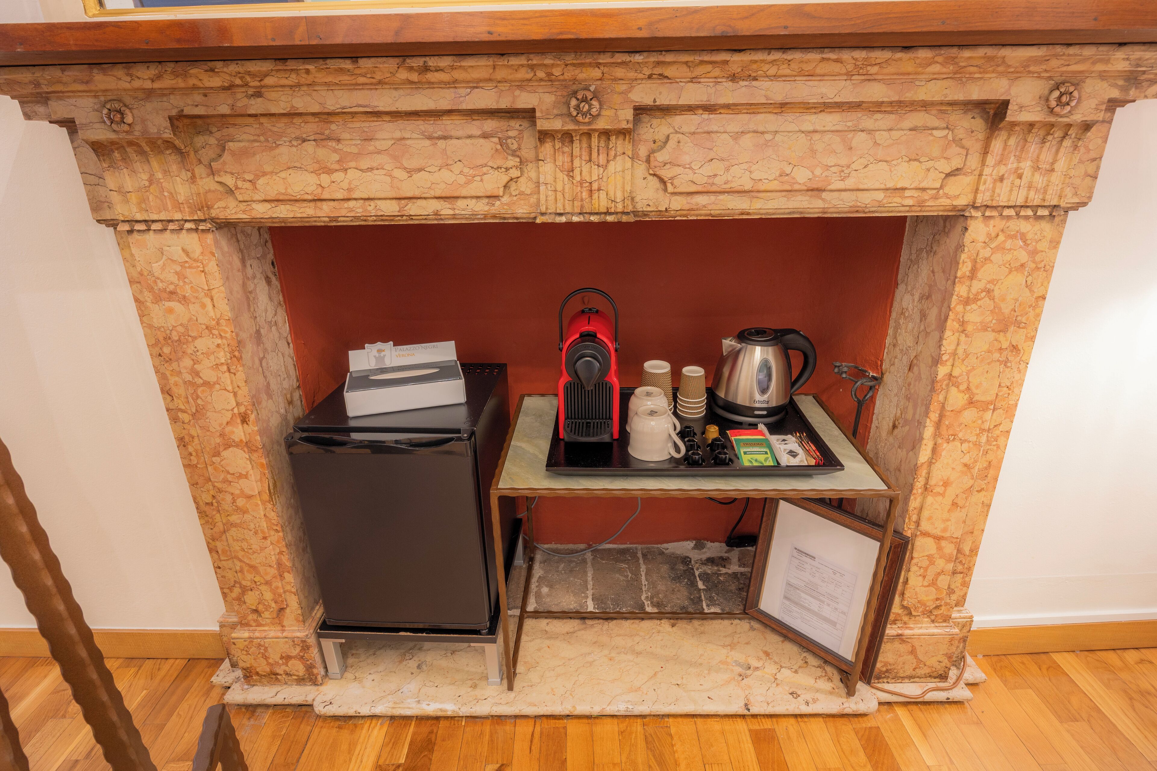 A kitchen area with a marble fireplace, a black refrigerator, and a small table with kitchen items.