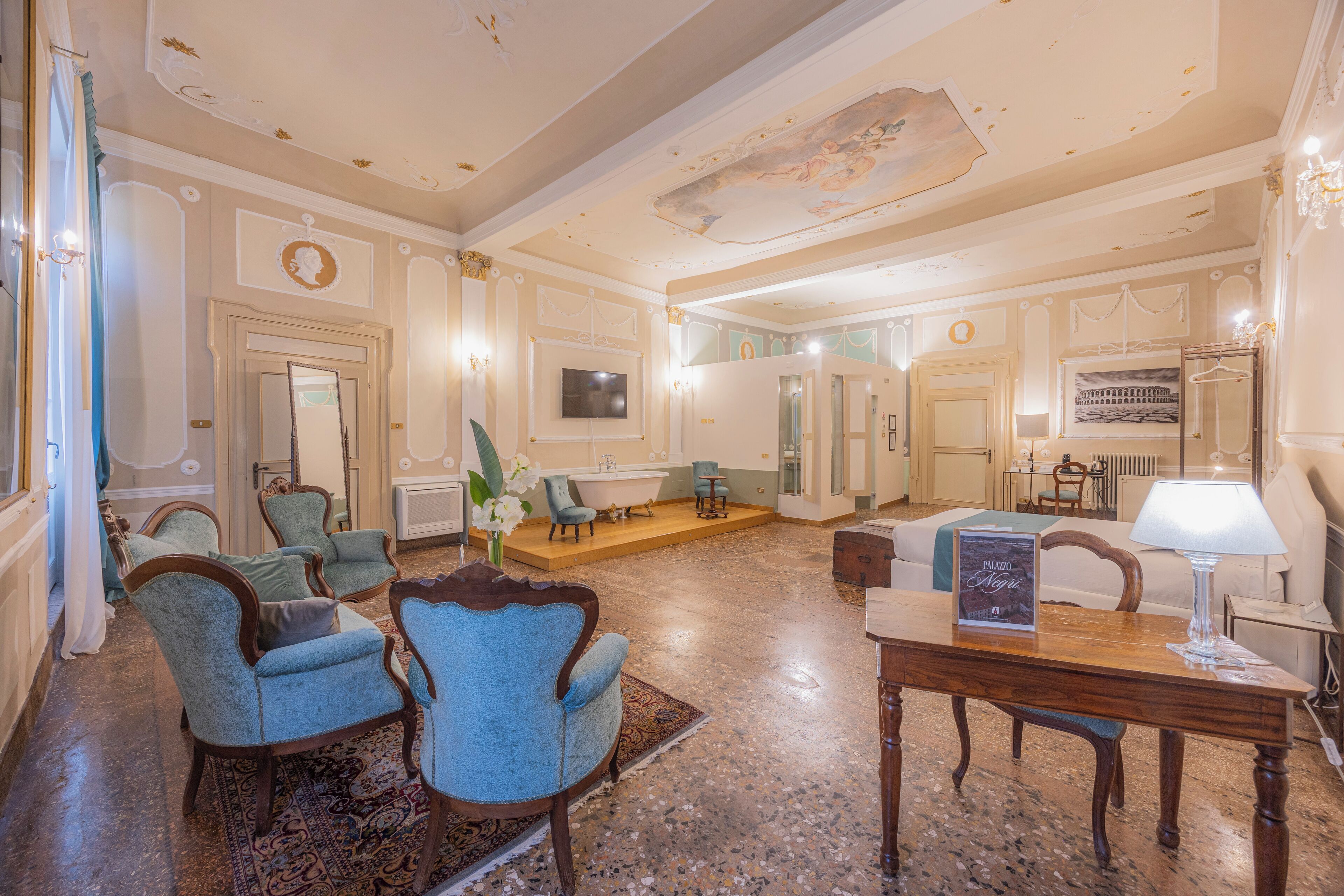 A spacious living room with a large wooden table, blue armchairs, a sofa, and a chandelier.