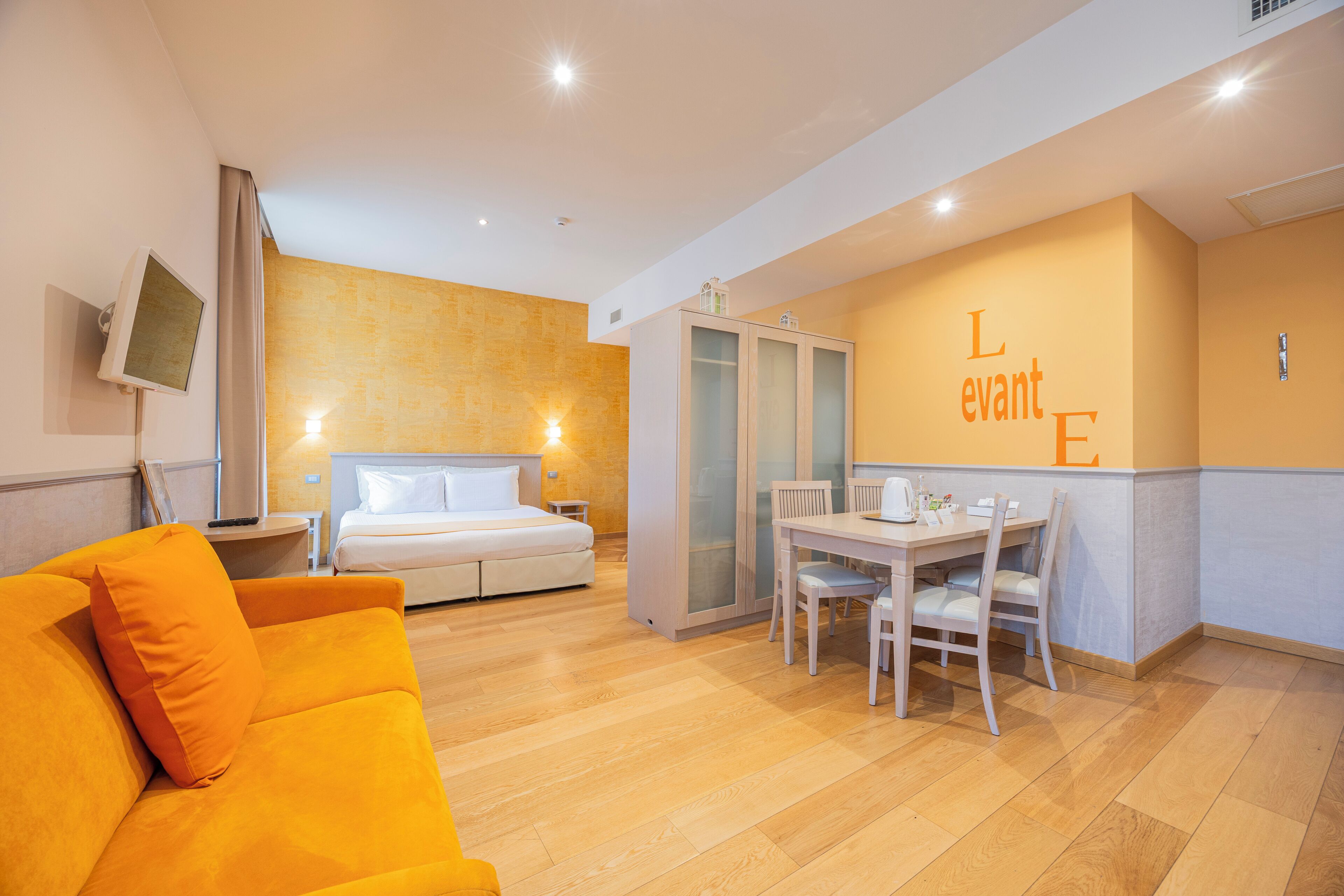 Une chambre d’hôtel comprenant un lit, une table à manger avec des chaises, un canapé et un téléviseur fixé au mur.