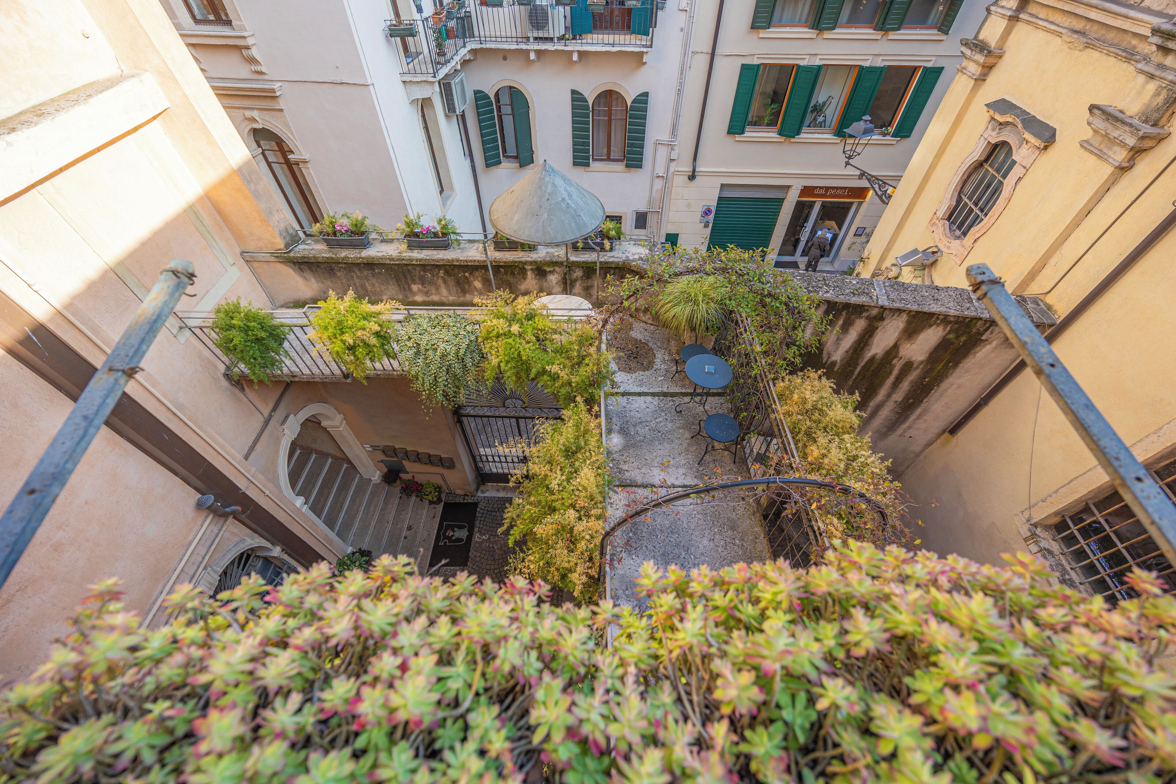 Un estrecho callejón flanqueado por edificios, con balcones adornados con plantas y una pequeña mesa con una silla.