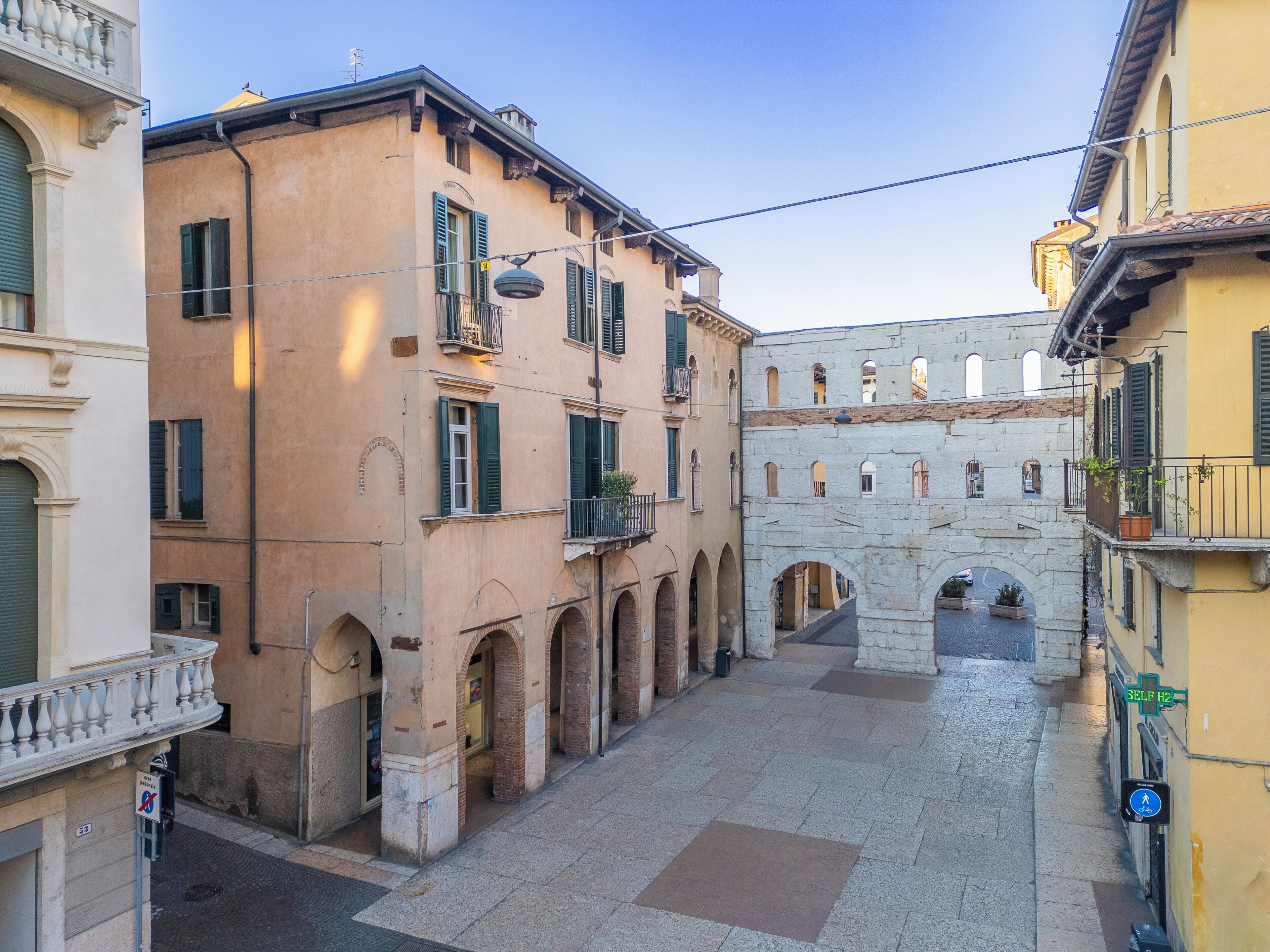 A narrow street with historic buildings, a stone archway, and a pedestrian path.