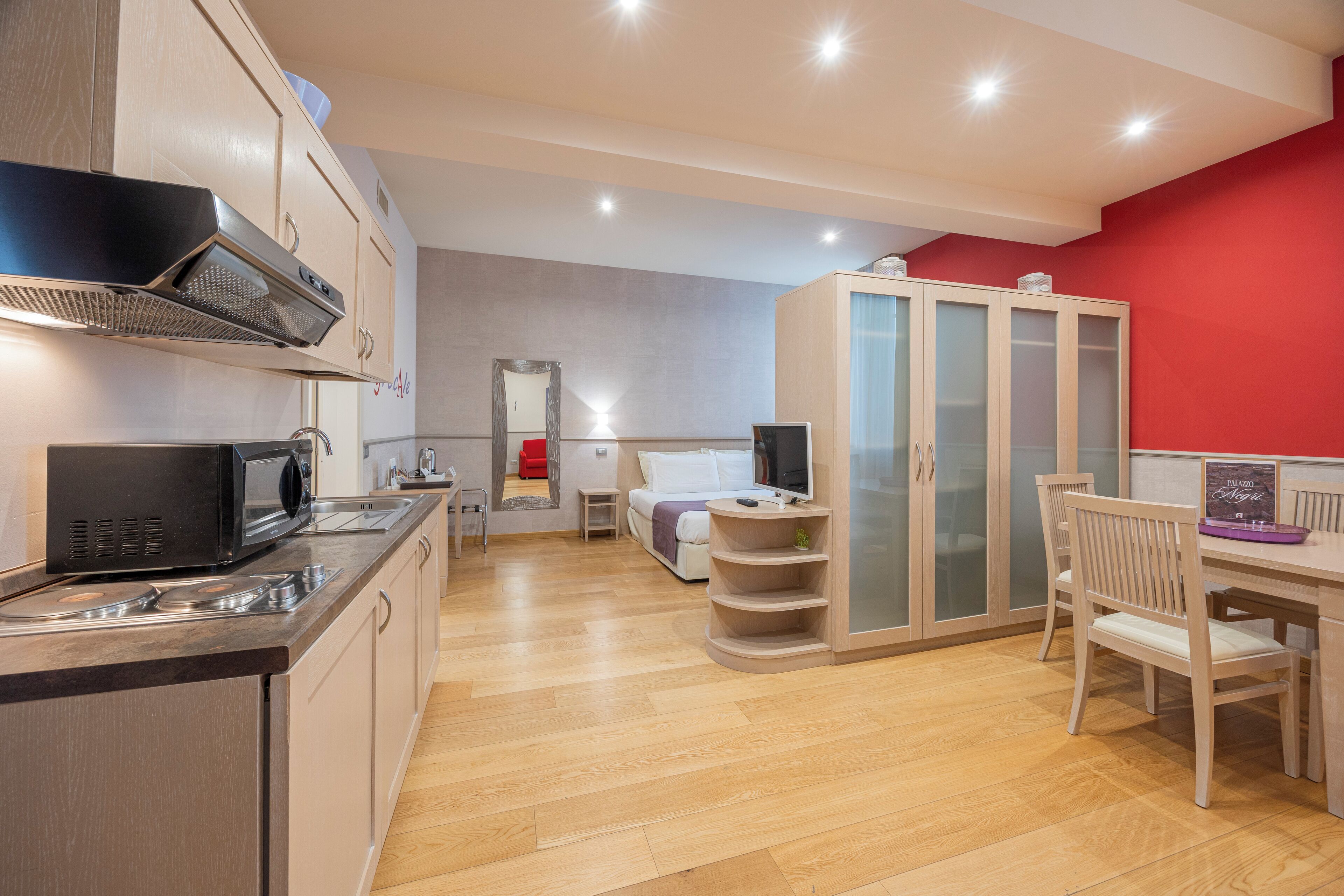 Eine moderne Küche mit Mikrowelle, Herd und Schränken. Es gibt eine Essecke mit Tisch und Stühlen. Im Hintergrund ist ein Kleiderschrank mit Schiebetüren zu sehen.