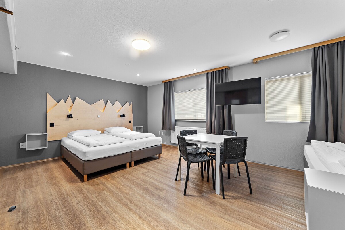 A modern hotel room with a bed, a desk, and a TV.