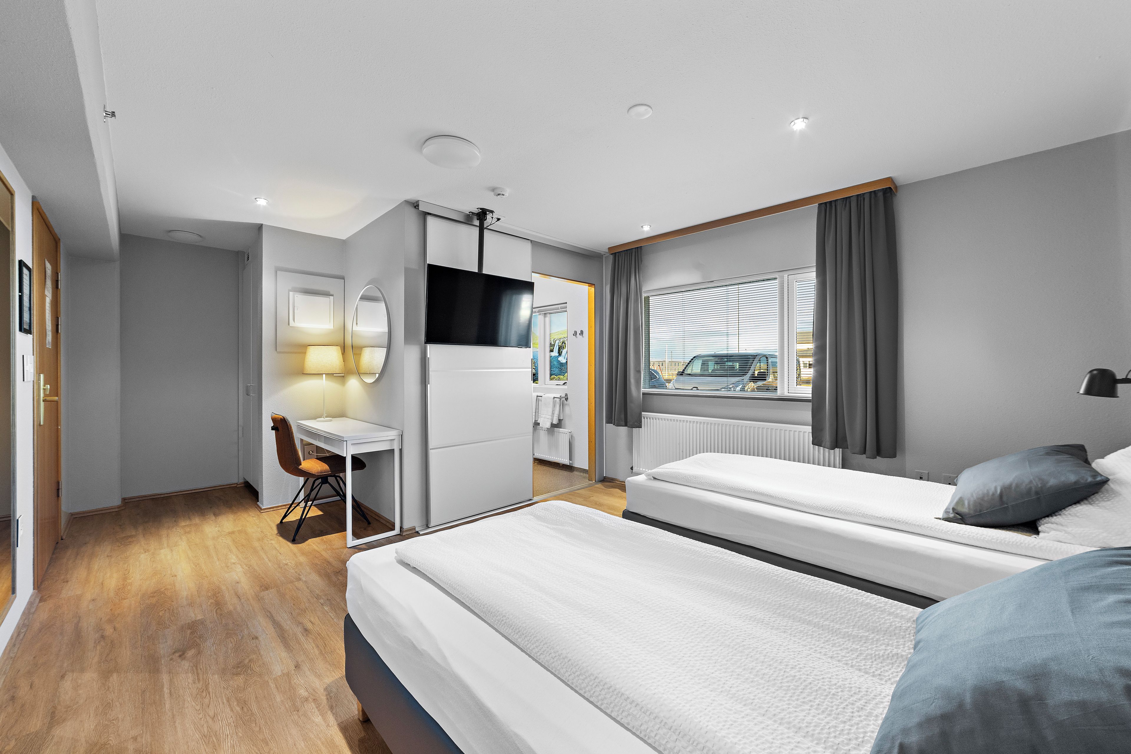 A modern hotel room with a bed, desk, and a view of the outside.