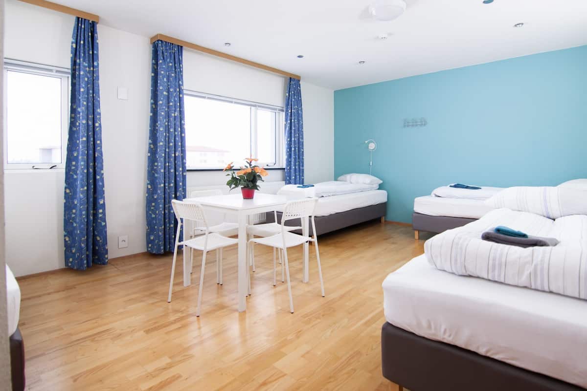 A modern bedroom with a bed, a small table with chairs, and a window with curtains.