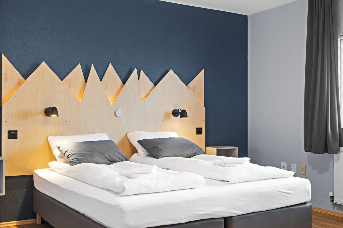 A hotel room with a bed, two bedside tables, a headboard with a geometric design, and a window with curtains.